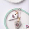 Concrete gem pendants with colorful logo design on pink and gold chains displayed on a white and mint green background